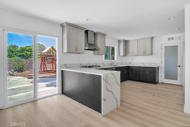 7812 Fairchild Ave, Winnetka, CA 91306 - kitchen featuring wall chimney exhaust hood, gray cabinets, gas stovetop, light wood-style floors, and light stone counters