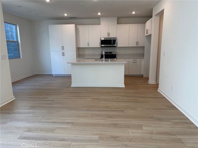 15929 Blue Copper Way, Fontana, CA 92336 - kitchen with stainless steel microwave, light countertops, white cabinets, light wood-style flooring, and a center island with sink