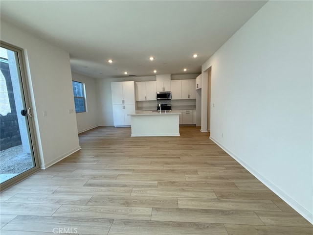 15929 Blue Copper Way, Fontana, CA 92336 - kitchen featuring stainless steel microwave, light wood-style floors, white cabinets, recessed lighting, and a center island with sink