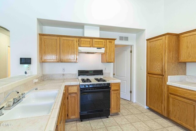 4810 Bluestone Dr, Bakersfield, CA 93311 - kitchen with gas range oven, under cabinet range hood, tile countertops, and brown cabinetry