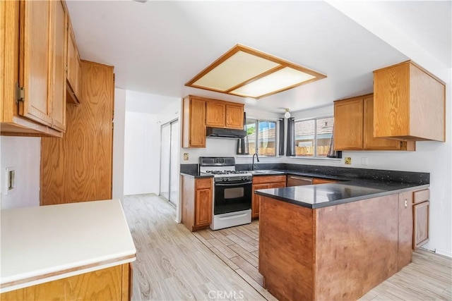 44738 Foxboro Ct, Lancaster, CA 93535 - kitchen featuring white gas stove, a peninsula, under cabinet range hood, light wood-type flooring, and brown cabinetry