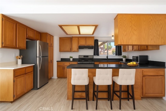44738 Foxboro Ct, Lancaster, CA 93535 - kitchen with stainless steel appliances, under cabinet range hood, brown cabinets, a kitchen bar, and light wood-style flooring