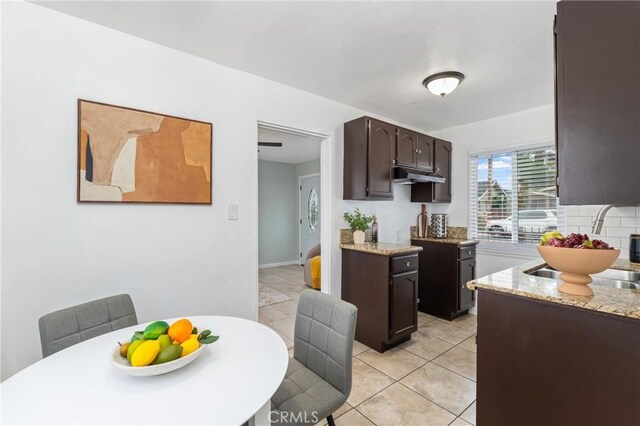 1048 S Record Ave, East Los Angeles, CA 90023 - kitchen featuring dark brown cabinetry, under cabinet range hood, light tile patterned flooring, tasteful backsplash, and light stone counters