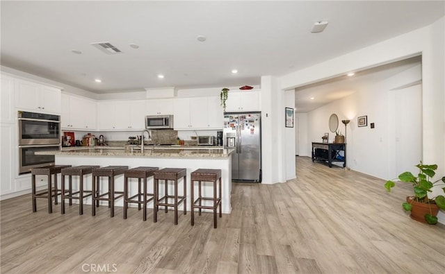 10963 Clementine Way, Loma Linda, CA 92354 - kitchen featuring stainless steel appliances, light wood finished floors, a kitchen breakfast bar, white cabinets, and an island with sink