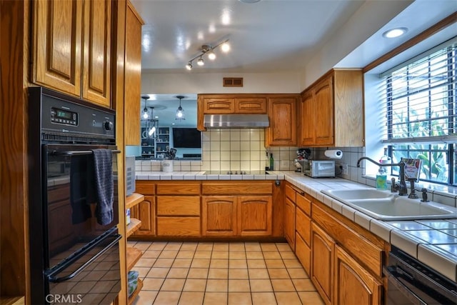 1853 E Renshaw St, Covina, CA 91724 - kitchen featuring brown cabinets, under cabinet range hood, decorative backsplash, light tile patterned floors, and tile counters