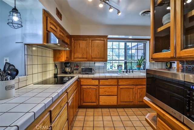 1853 E Renshaw St, Covina, CA 91724 - kitchen featuring black electric cooktop, tile countertops, brown cabinets, backsplash, and light tile patterned floors