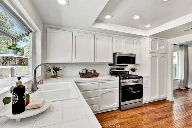 3401 Mountainside Cir, Corona, CA 92882 - kitchen featuring appliances with stainless steel finishes, tile countertops, white cabinets, a tray ceiling, and recessed lighting