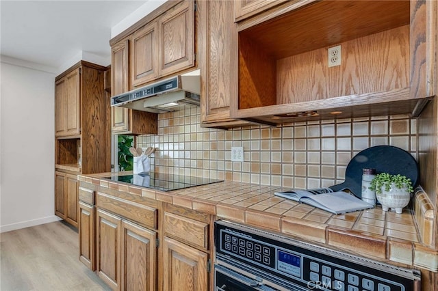 5856 E Scrivener St, Long Beach, CA 90808 - kitchen featuring tile counters, under cabinet range hood, decorative backsplash, black electric cooktop, and light wood-type flooring