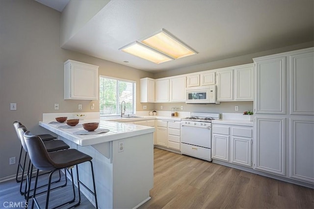 3087 Arbor Glen Ct, Corona, CA 92879 - kitchen featuring white appliances, a peninsula, light wood-style flooring, white cabinetry, and a kitchen breakfast bar