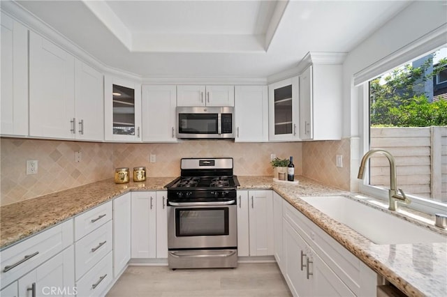 35 Havenwood Unit 83, Irvine, CA 92614 - kitchen featuring stainless steel appliances, white cabinets, light wood-style flooring, a tray ceiling, and glass insert cabinets