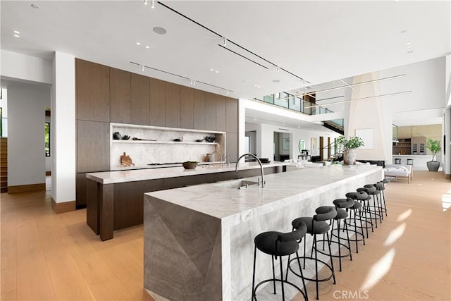 25151 Jim Bridger Rd, Hidden Hills, CA 91302 - kitchen featuring modern cabinets, a large island with sink, open floor plan, light wood-type flooring, and a breakfast bar area