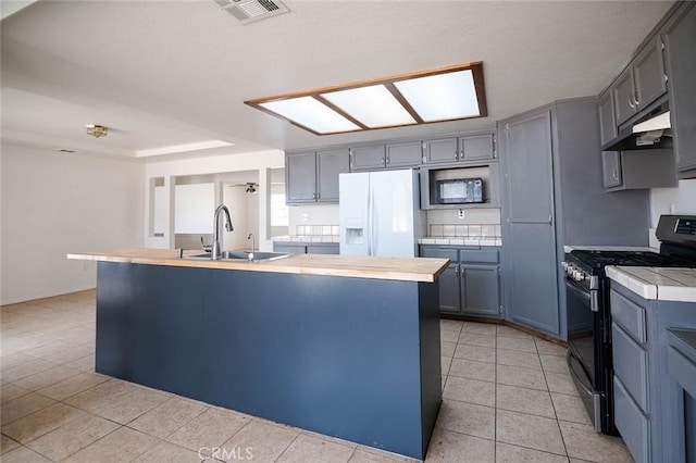 9018 Buckthorn Ave, Hesperia, CA 92345 - kitchen featuring black gas range oven, white refrigerator with ice dispenser, under cabinet range hood, light tile patterned flooring, and built in microwave