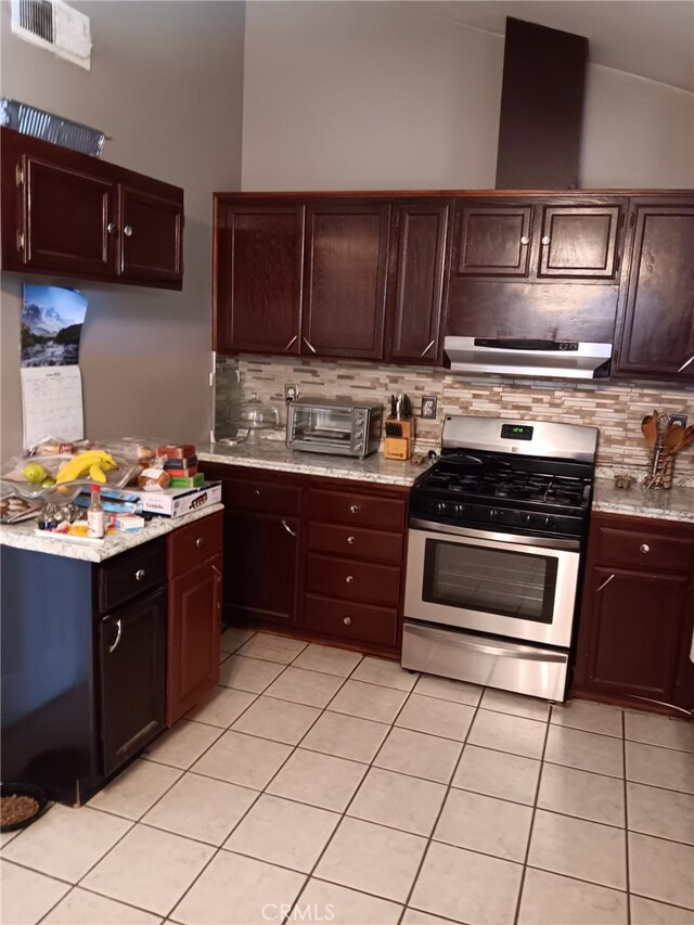412 Leeta St, Bakersfield, CA 93307 - kitchen with stainless steel gas stove, under cabinet range hood, light tile patterned floors, backsplash, and vaulted ceiling