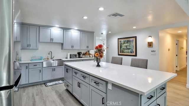 10361 Perdido St, Anaheim, CA 92804 - kitchen with stainless steel fridge, gray cabinets, light countertops, light wood-type flooring, and a center island