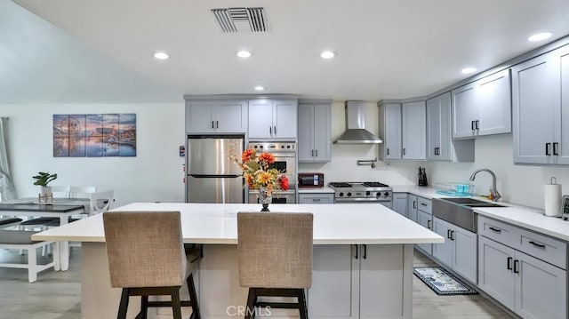 10361 Perdido St, Anaheim, CA 92804 - kitchen featuring appliances with stainless steel finishes, wall chimney exhaust hood, gray cabinetry, light wood finished floors, and a center island