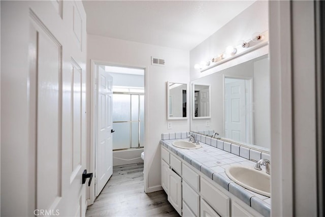 3807 Paula Ln, Lancaster, CA 93535 - bathroom featuring wood finished floors, double vanity, and bath / shower combo with glass door