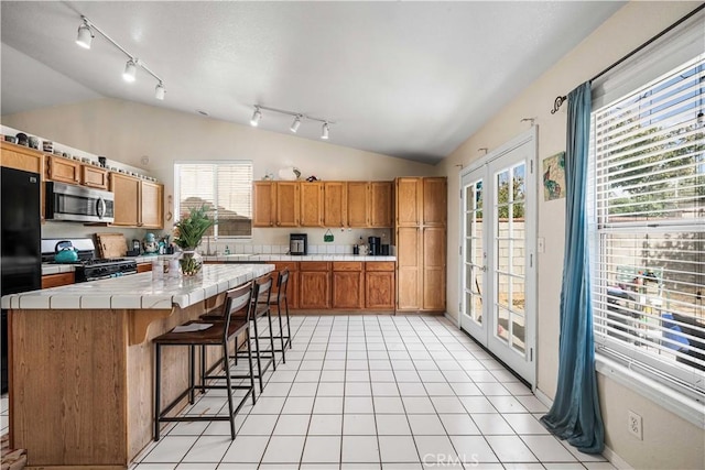 3038 Kaylyn St, Lancaster, CA 93535 - kitchen featuring stainless steel microwave, gas range oven, tile counters, lofted ceiling, and track lighting