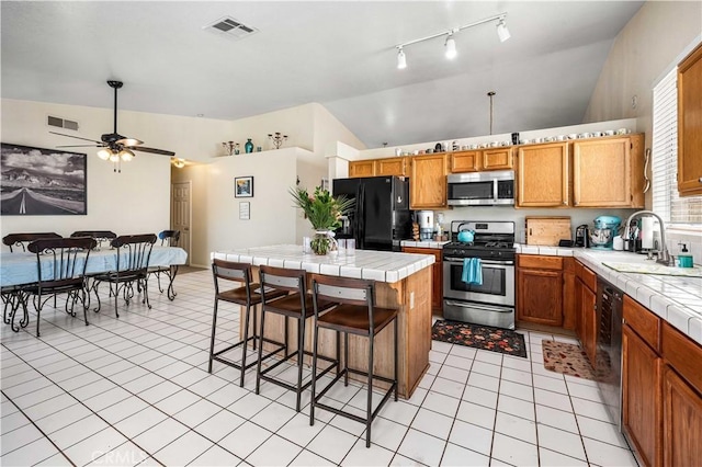 3038 Kaylyn St, Lancaster, CA 93535 - kitchen featuring appliances with stainless steel finishes, tile countertops, lofted ceiling, light tile patterned floors, and a kitchen bar