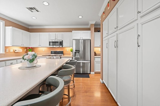 5191 Cobalt Way, Oceanside, CA 92057 - kitchen with appliances with stainless steel finishes, white cabinets, crown molding, a kitchen breakfast bar, and light countertops