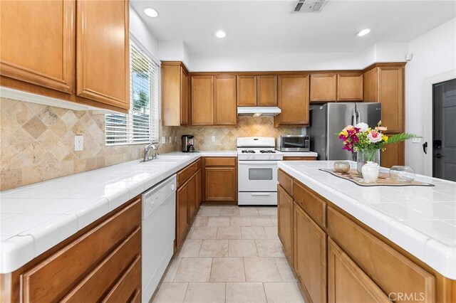 15216 Masline St, Baldwin Park, CA 91706 - kitchen featuring appliances with stainless steel finishes, under cabinet range hood, brown cabinets, tasteful backsplash, and recessed lighting