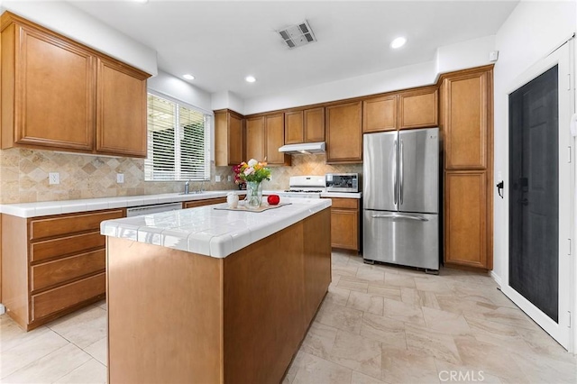 15216 Masline St, Baldwin Park, CA 91706 - kitchen with appliances with stainless steel finishes, under cabinet range hood, brown cabinets, tile countertops, and tasteful backsplash