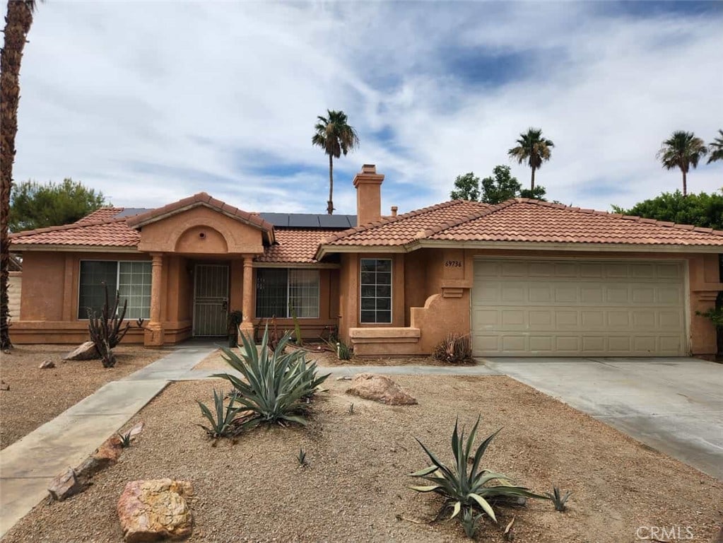 69736 Cypress Rd, Cathedral City, CA 92234 - view of front of home with an attached garage, driveway, stucco siding, a tiled roof, and solar panels