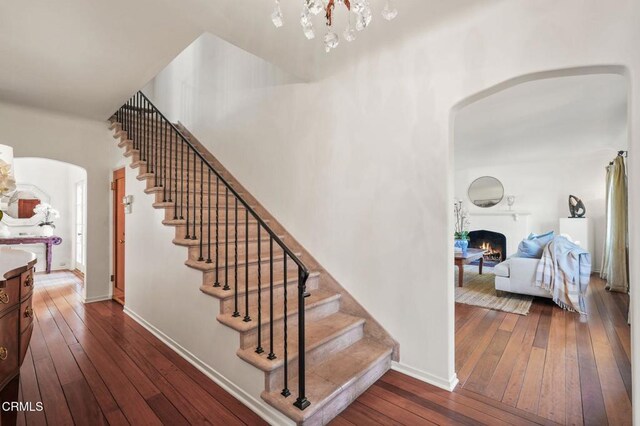 980 El Campo Dr, Pasadena, CA 91107 - staircase featuring arched walkways, hardwood / wood-style flooring, a chandelier, and a warm lit fireplace