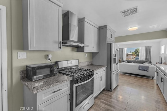 74417 Maricopa Dr Unit 29, Palms, CA 92277 - kitchen featuring appliances with stainless steel finishes, wall chimney exhaust hood, open floor plan, wood finished floors, and light stone countertops