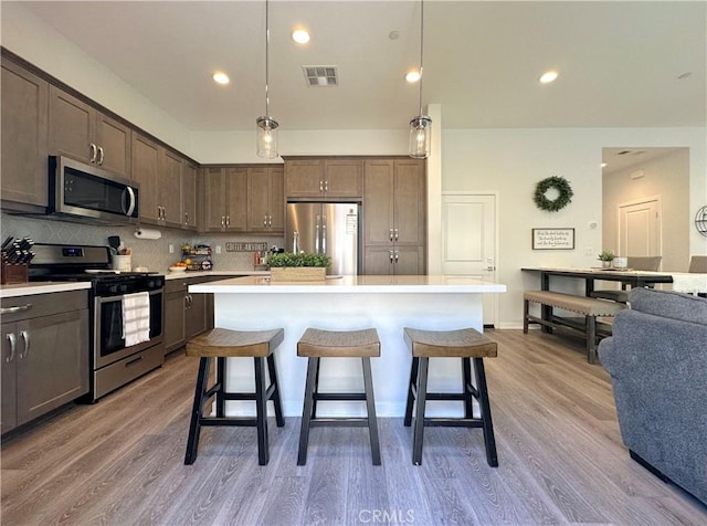 4173 Horvath St Unit 104, Corona, CA 92883 - kitchen with appliances with stainless steel finishes, tasteful backsplash, a breakfast bar area, a kitchen island, and light wood-style flooring