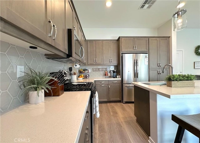 4173 Horvath St Unit 104, Corona, CA 92883 - kitchen with stainless steel appliances, light wood finished floors, light countertops, a kitchen breakfast bar, and tasteful backsplash