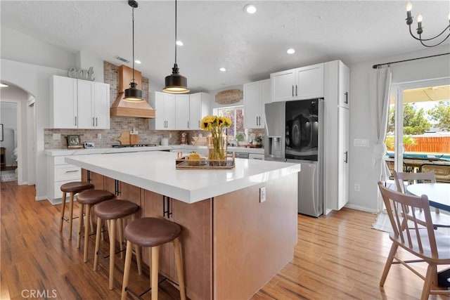 7733 Pismo Ave, Hesperia, CA 92345 - kitchen featuring stainless steel refrigerator with ice dispenser, a center island, arched walkways, tasteful backsplash, and custom range hood