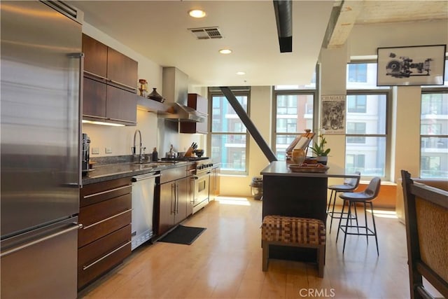 207 Broadway E Unit 302, Long Beach, CA 90802 - kitchen featuring appliances with stainless steel finishes, wall chimney exhaust hood, light wood-style floors, a breakfast bar area, and dark brown cabinets