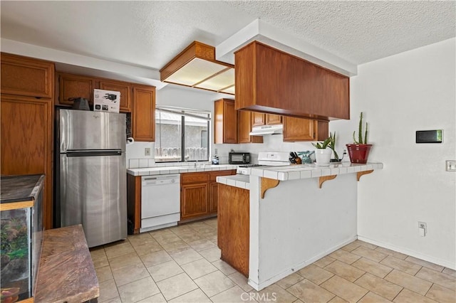 2021 Buckwheat Ave, Rosamond, CA 93560 - kitchen with freestanding refrigerator, white dishwasher, tile countertops, under cabinet range hood, and a peninsula