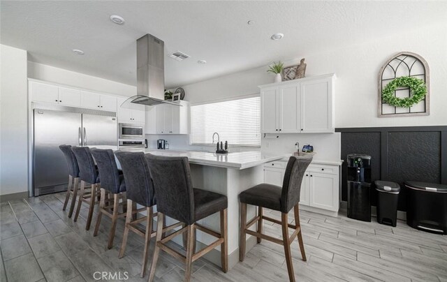 825 Spring St W, Madera, CA 93636 - kitchen featuring built in appliances, island range hood, a kitchen island, a breakfast bar, and light countertops