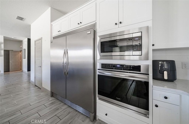 825 Spring St W, Madera, CA 93636 - kitchen featuring built in appliances, light wood-style floors, white cabinets, light stone countertops, and decorative backsplash