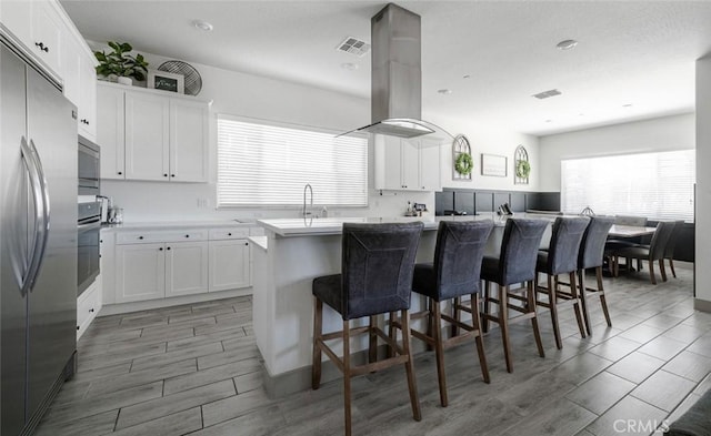 825 Spring St W, Madera, CA 93636 - kitchen featuring island range hood, white cabinetry, a breakfast bar area, and wood tiled floors