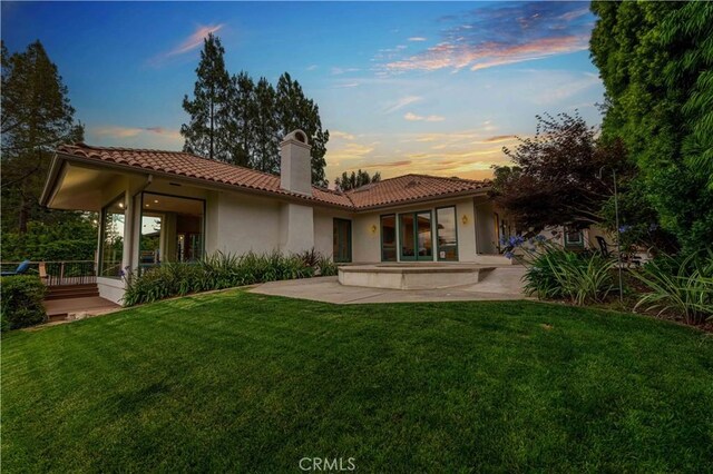 1525 Ramona Dr, Camarillo, CA 93010 - back of house at dusk with a chimney, a patio, a tile roof, stucco siding, and a lawn