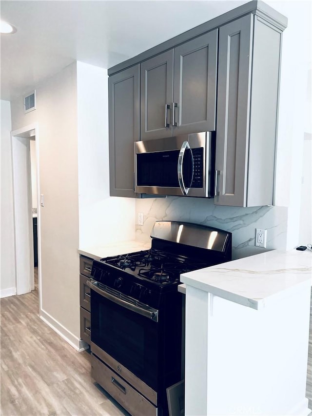 5126 Colfax Ave, Valley Village, CA 91601 - kitchen featuring range with gas stovetop, stainless steel microwave, light wood-style floors, tasteful backsplash, and light stone counters