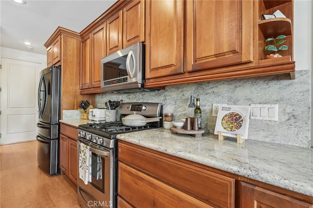 11272 Weatherby Rd, Los Alamitos, CA 90720 - kitchen featuring appliances with stainless steel finishes, brown cabinetry, light stone counters, open shelves, and light wood finished floors