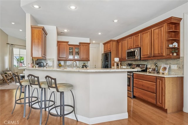 11272 Weatherby Rd, Los Alamitos, CA 90720 - kitchen featuring appliances with stainless steel finishes, a peninsula, light wood-type flooring, brown cabinets, and a breakfast bar area