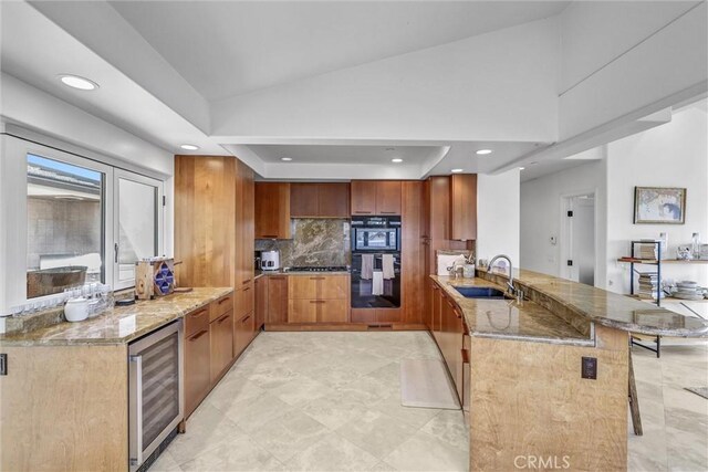 34586 Camino Capistrano Unit A, Dana Point, CA 92624 - kitchen with wine cooler, a peninsula, light stone counters, brown cabinets, and decorative backsplash