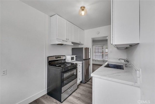 122 Elm Ave Unit 11, Long Beach, CA 90802 - kitchen featuring stainless steel appliances, under cabinet range hood, light wood-style floors, white cabinetry, and light stone counters