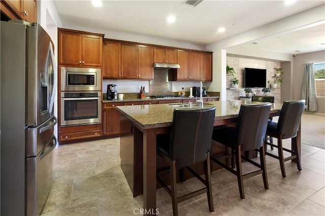 28233 Millstream Ct, Menifee, CA 92585 - kitchen with stainless steel appliances, under cabinet range hood, brown cabinetry, a kitchen bar, and recessed lighting
