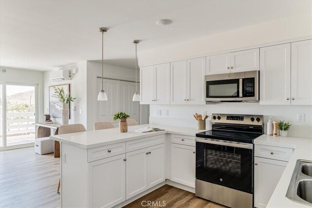3802 Ranch House Rd Unit 102, San Luis Obispo, CA 93401 - kitchen with stainless steel appliances, a wall mounted air conditioner, a peninsula, wood finished floors, and white cabinets