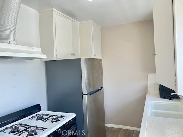 122 Elm Ave Unit 9, Long Beach, CA 90802 - kitchen with white gas range oven, white cabinets, wall chimney range hood, and wood finished floors