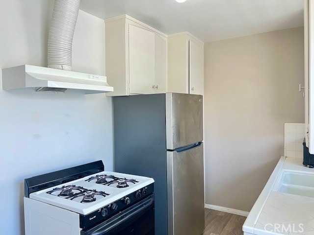 122 Elm Ave Unit 9, Long Beach, CA 90802 - kitchen featuring white gas range, wall chimney range hood, tile countertops, light wood finished floors, and white cabinetry
