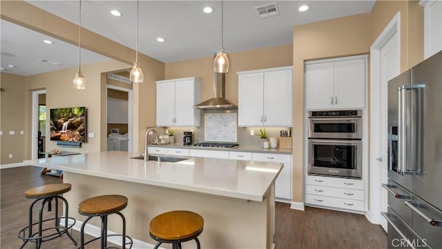 126 Luneta Ln, Rancho Mission Viejo, CA 92694 - kitchen with appliances with stainless steel finishes, dark wood-style flooring, wall chimney exhaust hood, a kitchen bar, and white cabinets