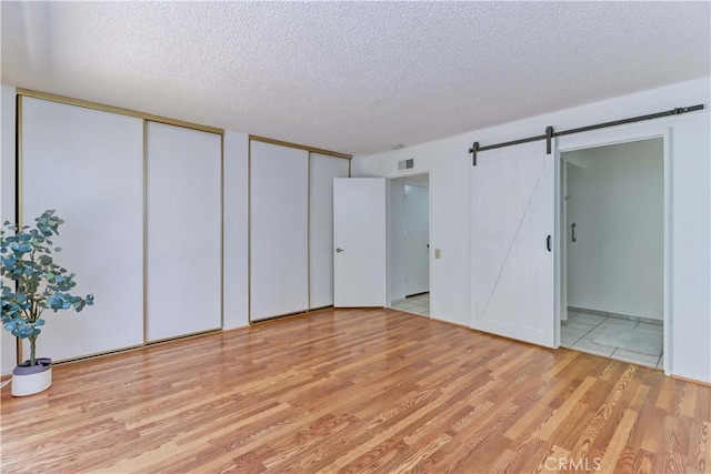 3463 Bahia Blanca W Unit B, Laguna Woods, CA 92637 - unfurnished bedroom featuring multiple closets, a barn door, a textured ceiling, light wood finished floors, and ensuite bath