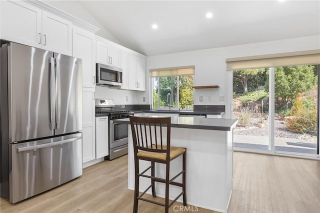24538 Meadow Grass Way, Moreno Valley, CA 92557 - kitchen featuring stainless steel appliances, dark countertops, white cabinetry, a kitchen island, and vaulted ceiling