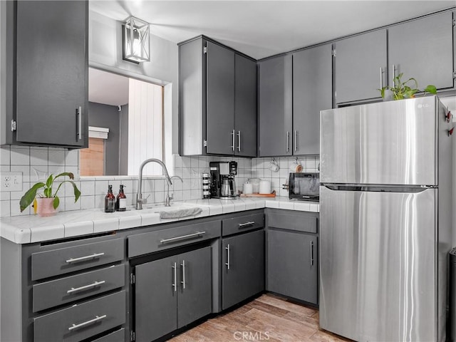 17789 Sycamore St, Hesperia, CA 92345 - kitchen featuring freestanding refrigerator, gray cabinetry, backsplash, and light wood-style floors